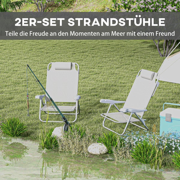 Set aus zwei klappbaren Strandstühlen mit Kopfkissen auf einer Wiese am Wasser neben einer Angelrute und einer Kühlbox.