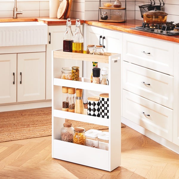 Schmaler, weißer Küchenwagen mit drei Ablagen und diversen Vorratsbehältern vor einer weißen Küchenzeile.