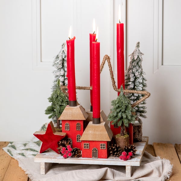 Adventsgesteck mit roten Kerzen, Holzdekoration und kleinen Weihnachtsbäumen auf einem Tisch