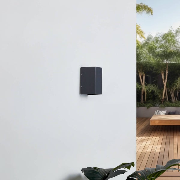 Moderne Außenwandleuchte in Anthrazit an einer weißen Wand auf einer hellen Terrasse mit Holzdeck und Pflanzen.