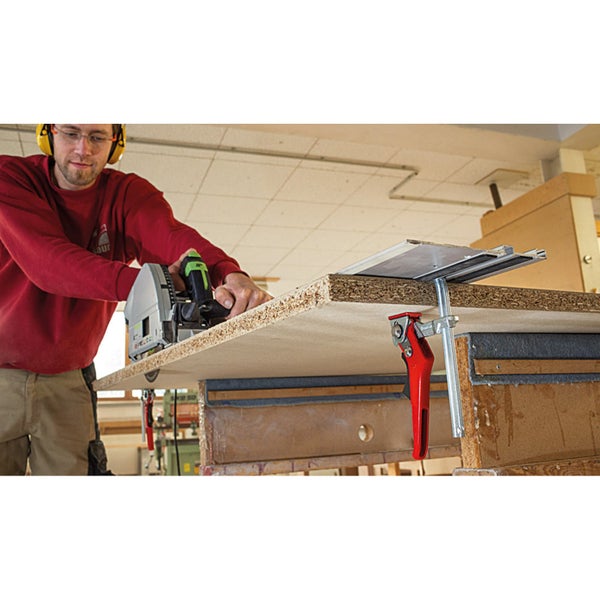 Ein Mann benutzt eine Tauchsäge zum Schneiden einer Holzplatte, die mit Schraubzwingen befestigt ist.