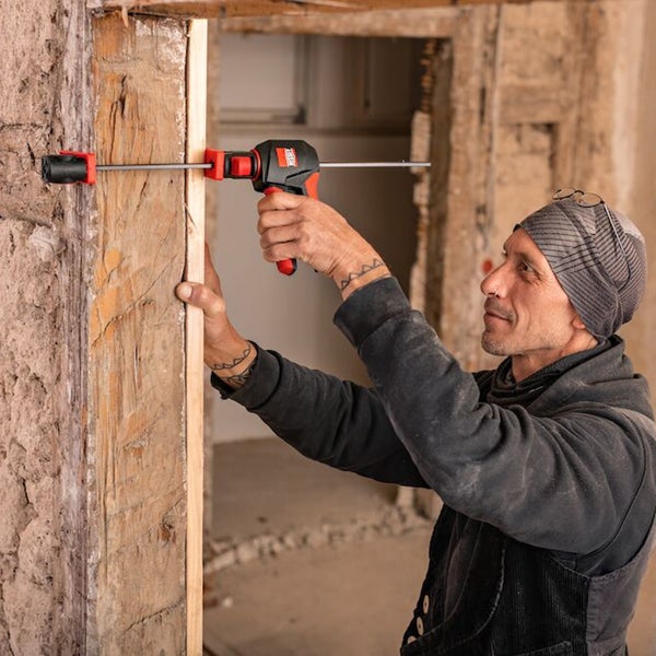Handwerker befestigt Holz mit einer Einhandzwinge an einem Türrahmen