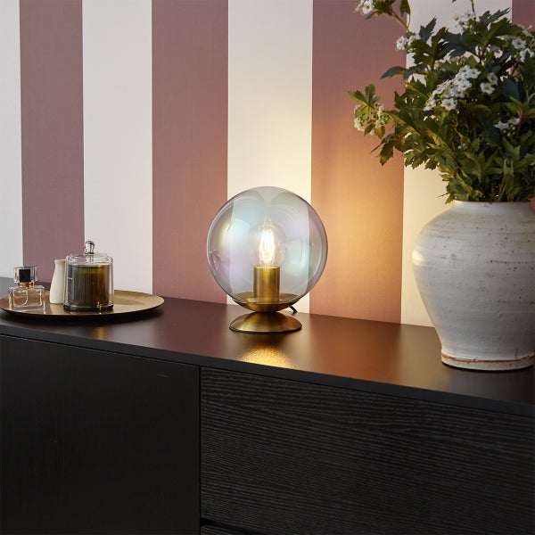 Moderne Tischleuchte mit kugelförmigem, irisierendem Glasschirm und Messingfuß auf einem dunklen Sideboard.