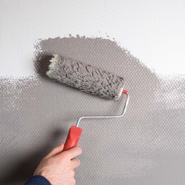 Strukturierte Tapete mit feinem Webmuster an einer Wand hinter dekorativen Vasen auf einem Tisch in einem hellen, modern gestalteten Raum.