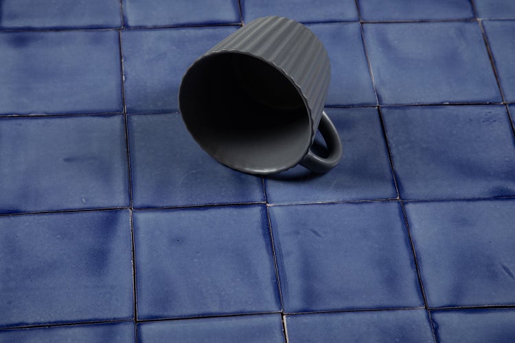 Graue Tasse auf blauem Keramikfliesenboden