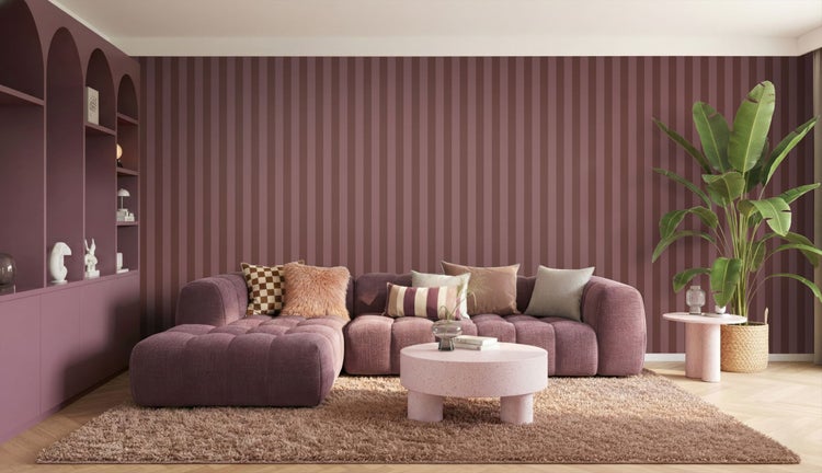 Wohnzimmer mit lila Sofa, verschiedenen Kissen, runder Couchtisch auf Hochflor-Teppich, gestreifte Tapete und eine große Zimmerpflanze.