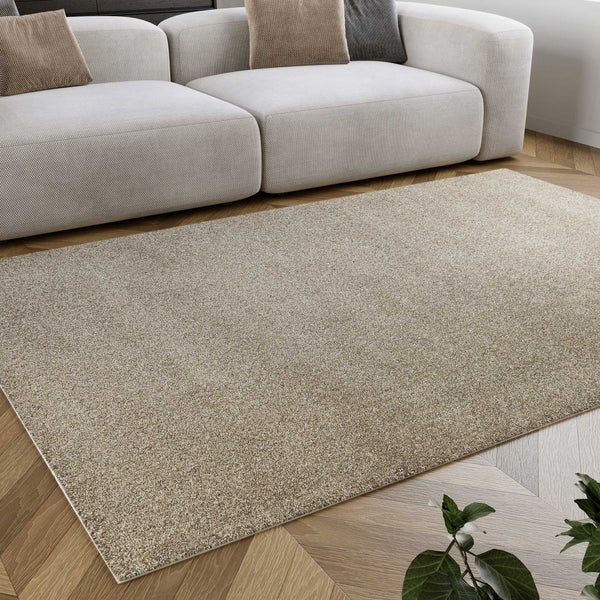 Rechteckiger Teppich mit melierter Struktur in einem hellen Wohnzimmer auf Fischgrätparkett neben einem modernen Sofa.