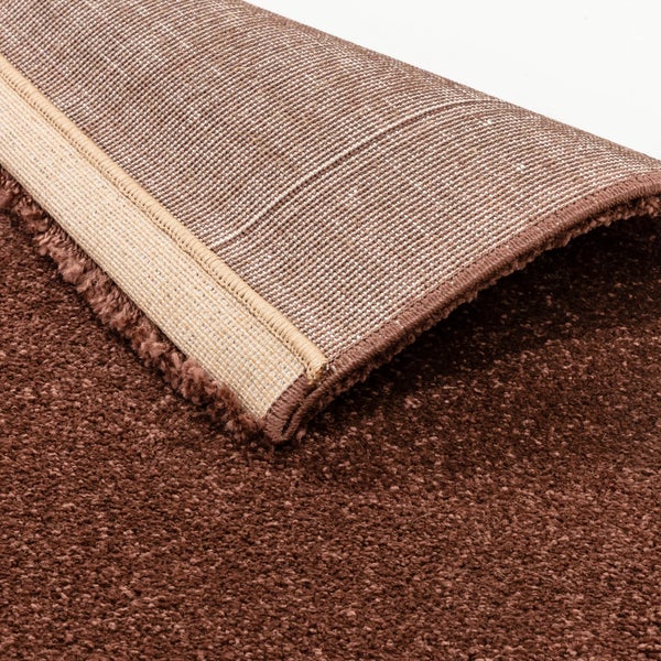 Hochflor-Teppich in Braun mit umgeschlagener Ecke und strukturierter Unterseite.