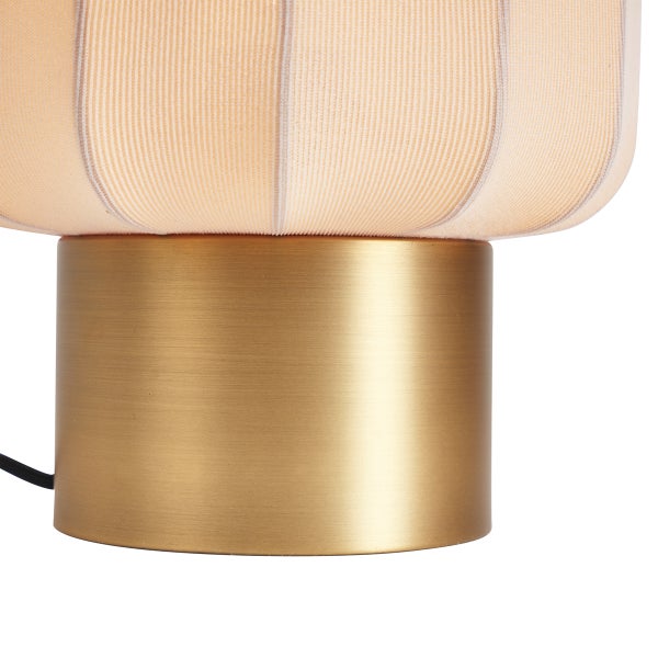 Detailansicht einer Tischlampe mit rundem Sockel aus gebürstetem Metall in Messingoptik und geripptem Stoffschirm.