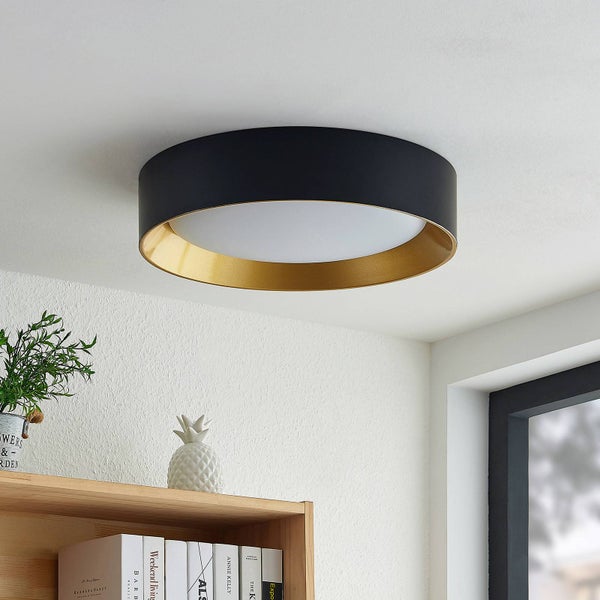 Runde Deckenleuchte mit schwarzem Außenrahmen und goldfarbenem Innenring an einer weißen Zimmerdecke über einem Regal.