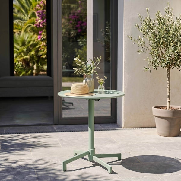 Runder Bistro-Gartentisch aus Metall auf einer hellen Terrasse mit Steinplatten, dekoriert mit Strohhut und Vasen.