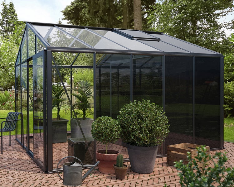 Modernes Gewächshaus mit dunklem Metallrahmen und Glaswänden auf einer Terrasse im Garten.