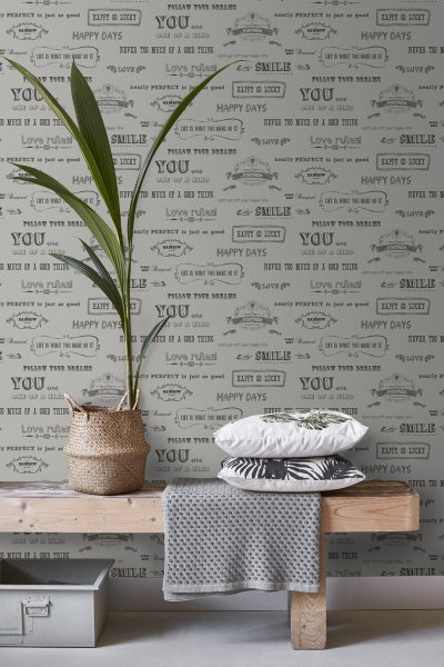 Dekorative Szene mit Zimmerpflanze, Kissen und Textilien vor einer Wandtapete mit Schriftzügen