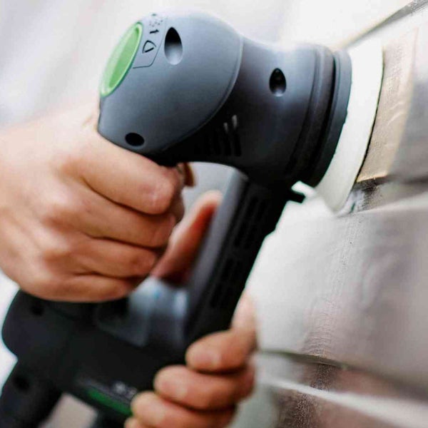 Eine Person schleift eine Holzoberfläche mit einem Exzenterschleifer.