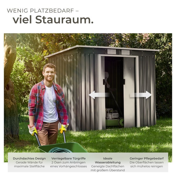 Anthrazitfarbenes Gerätehaus aus Metall mit Doppelschiebetüren in einem Garten. Ein Mann mit einer Schubkarre steht davor.