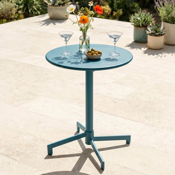 Runder Bistro-Tisch aus Metall auf einer hellen Terrasse, dekoriert mit Cocktailgläsern, Oliven und Blumen in einer modernen Umgebung.