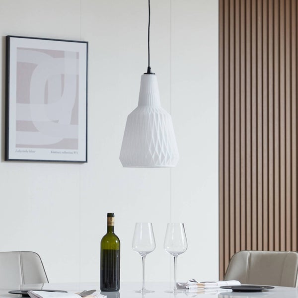 Weiße Pendelleuchte mit geometrischem Muster über einem Esstisch in einem modern gestalteten Raum mit Holzwandpaneel.