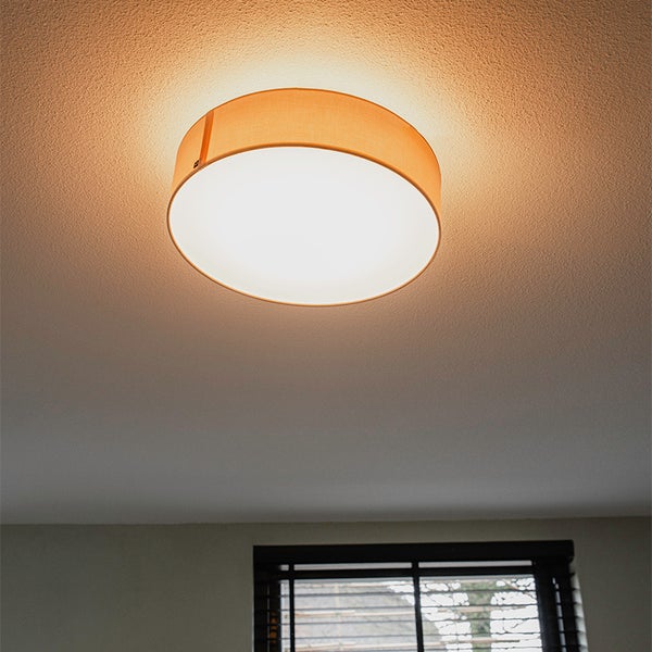 Runde Deckenleuchte mit Stoffschirm, eingeschaltet an einer strukturierten Decke.