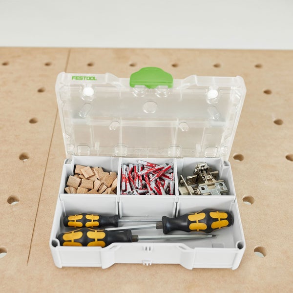Festool Organizer mit Fächern, Holzplättchen, Dübeln, Scharnieren und Schraubendrehern auf einem Arbeitstisch mit Lochraster.