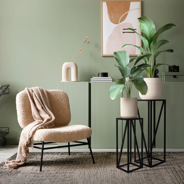 Einrichtungsszene mit modernem Teddy Sessel, Pflanzen auf schwarzen Metallständern und einem grünen Sideboard in einem gemütlichen Wohnbereich.