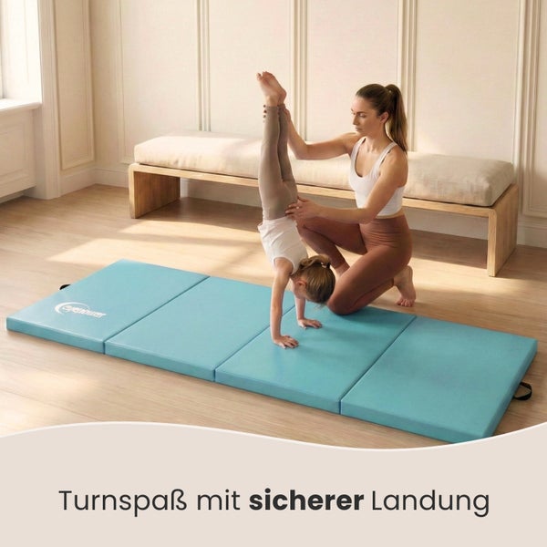 Mädchen macht Handstand auf einer blauen Gymnastikmatte mit Unterstützung einer Frau.