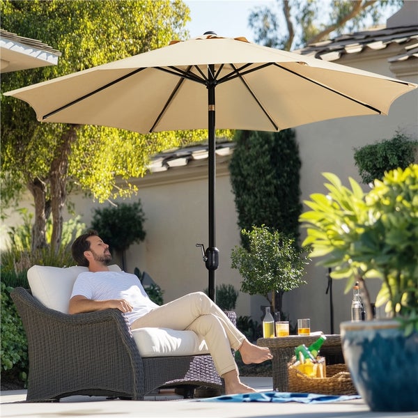 Szene im Freien mit einem Mann, der unter einem Sonnenschirm im Gartenmöbel sitzt.