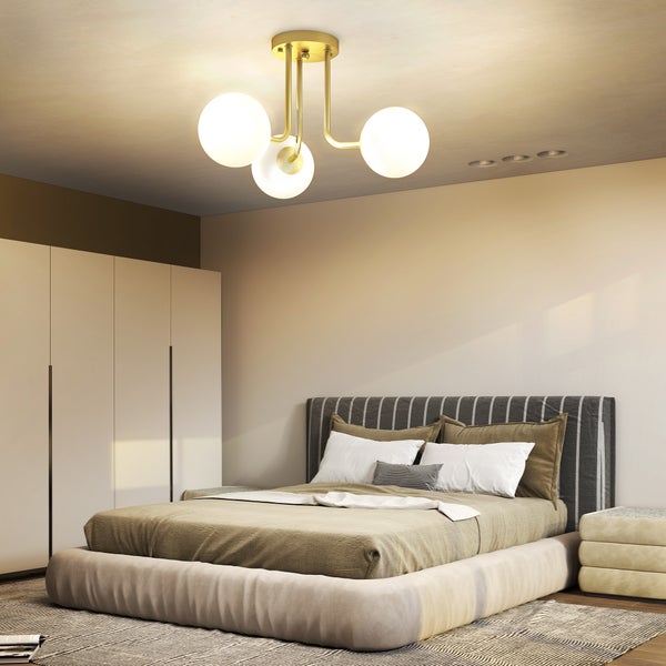 Moderne Deckenleuchte mit drei weißen Glaskugeln und goldfarbenem Metallgestell in einem hellen Schlafzimmer mit Bett und Kleiderschrank.