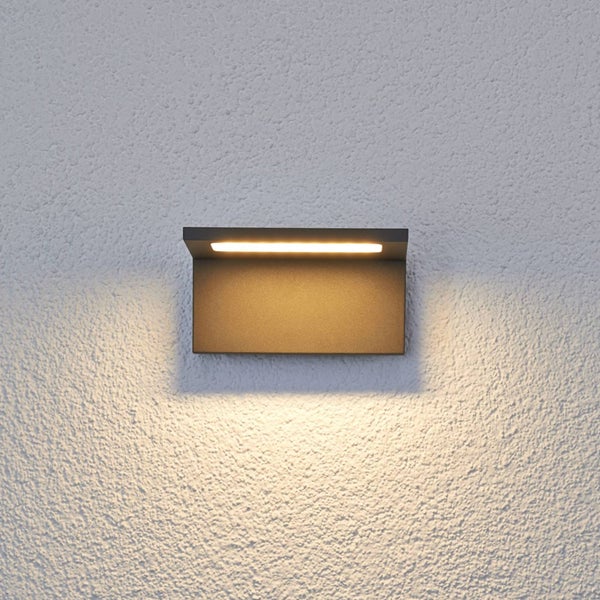 Moderne LED-Außenwandleuchte aus anthrazitfarbenem Metall mit warmweißem Lichtschein nach unten auf einer Putzwand.