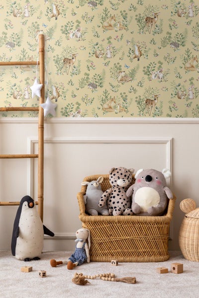 Kinderzimmer mit Vliestapete mit Waldtieren wie Rehen und Hasen, einer Bambusleiter und Plüschtieren in einem Weidenkorb auf hellem Teppichboden.