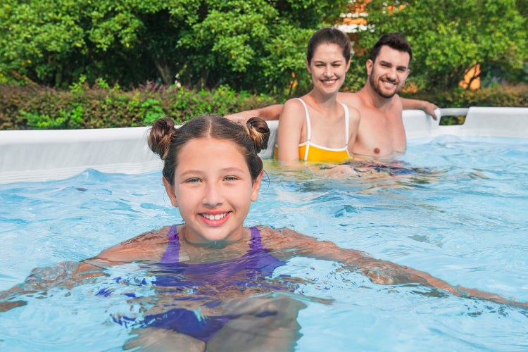 Familie mit Kind in einem Aufstellpool im Garten vor Bäumen und Sträuchern.