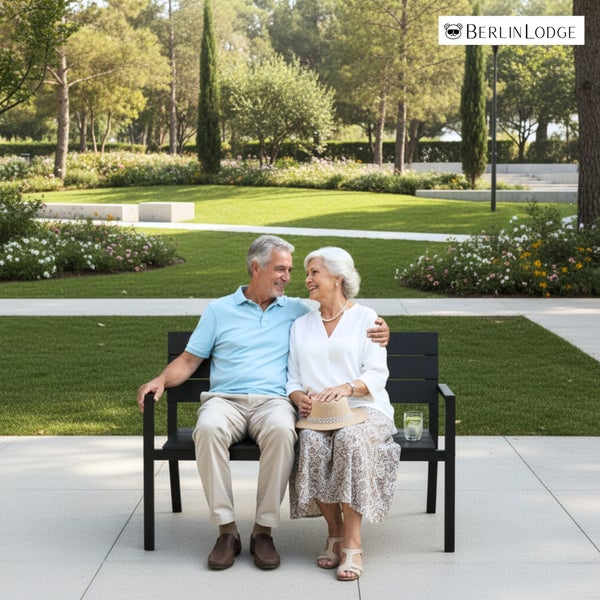 Ein Seniorenpaar sitzt auf einer schwarzen Gartenbank in einem gepflegten, weitläufigen Garten. Berlin Lodge Logo.