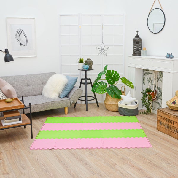 Gestreifte Puzzlematte aus Schaumstoff in Rosa und Grün in einem hellen Wohnzimmer mit grauem Sofa auf Laminatboden.