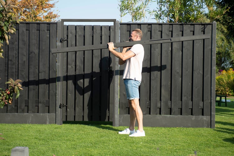 Mann trägt Holzzaunlatte vor Holzzaun im Garten