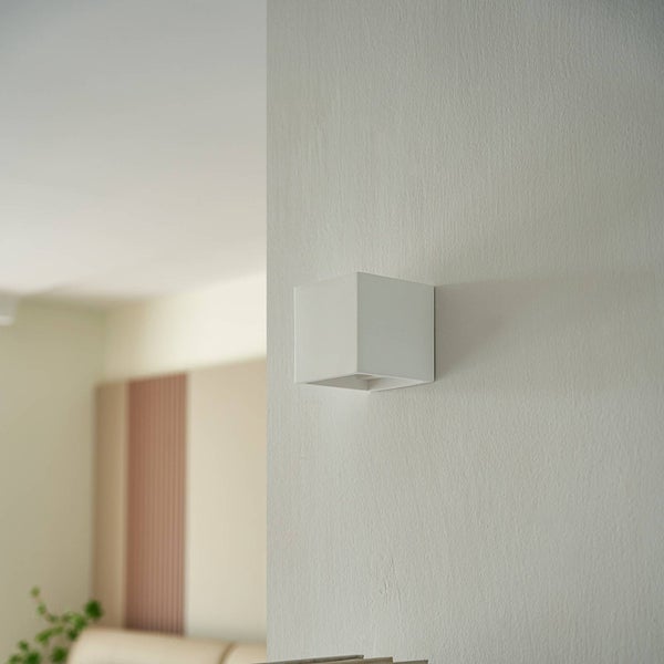 Moderne Wandleuchte in Würfelform an einer Zimmerwand in einem minimalistisch gestalteten, hellen Wohnraum.