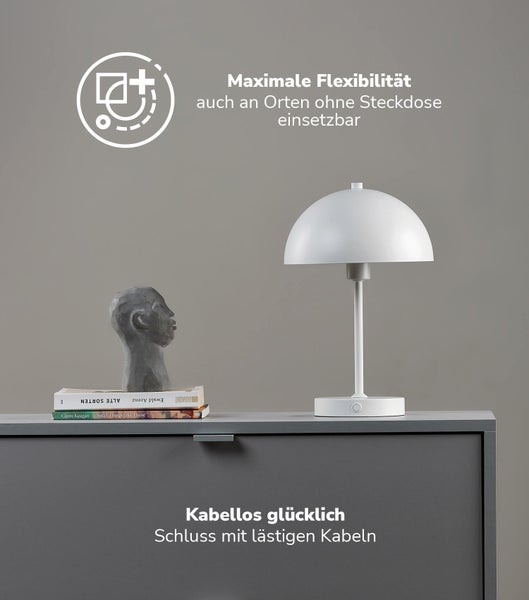 Akkubetriebene Tischleuchte mit halbkugelförmigem Schirm auf einer Kommode neben einer Skulptur und Büchern. Flexibel ohne Kabel einsetzbar.