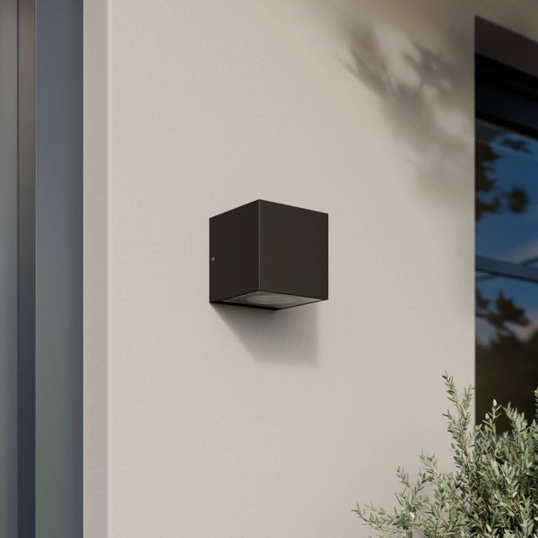 Moderne würfelförmige Außenwandleuchte in Anthrazit an einer Hauswand in einer hellen und modernen Umgebung.