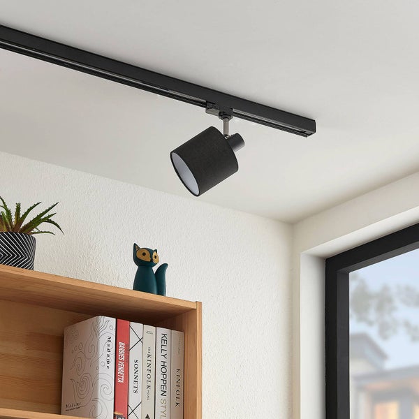 Schwarzer Schienensystem-Strahler mit Stoffschirm an einer schwarzen Deckenschiene über einem Regal mit Büchern.