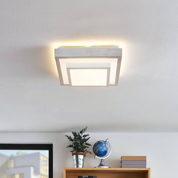 Quadratische LED Deckenleuchte in modernem, geometrischem Design an einer Decke über einem Holzregal mit Pflanze und Globus in einem hellen Raum.