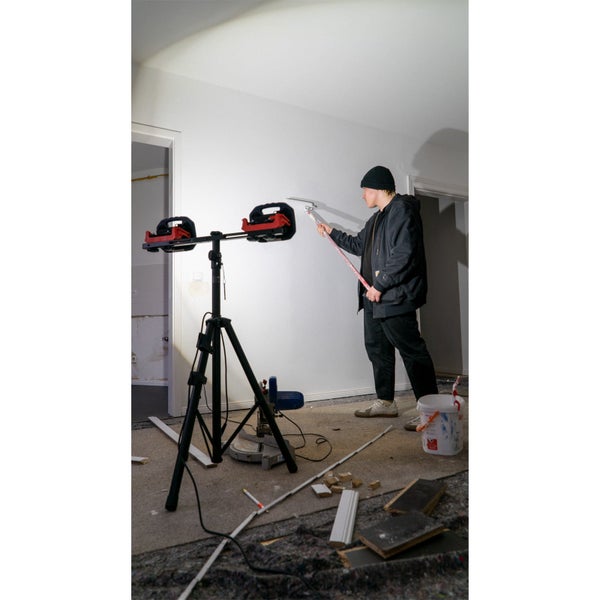 Handwerker glättet Wand mit Spachtel unter Licht eines Doppel-Baustrahlers auf Stativ in einem Raum während der Renovierung.