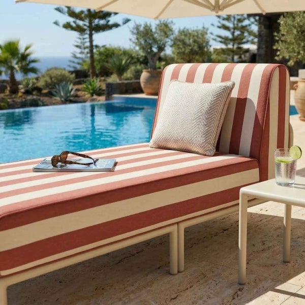 Gestreifte Gartenliege mit Kissen am Pool, daneben ein kleiner Beistelltisch in einer hellen Außenanlage.