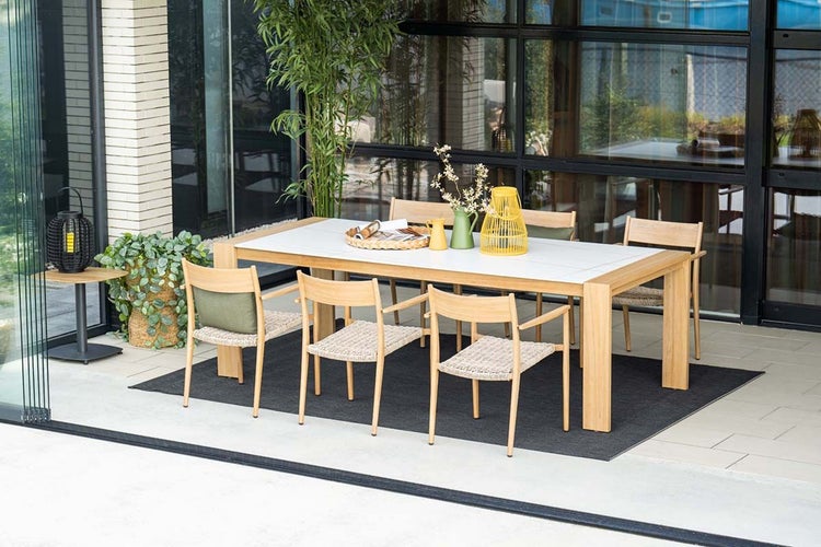 Moderner Essbereich im Freien mit einem großen Gartentisch aus Holz mit weißer Platte und sechs Holzstühlen auf einem Teppich auf einer Terrasse.