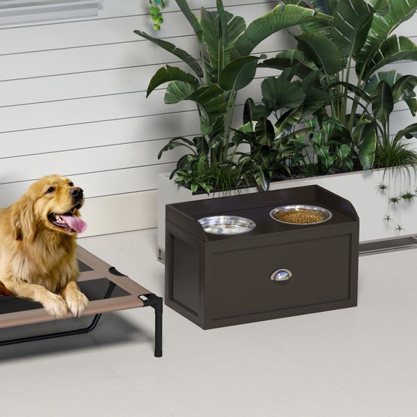 Futterstation aus dunklem Holz mit zwei Edelstahlnäpfen und Schublade, Golden Retriever auf einer Hundeliege in heller Umgebung.