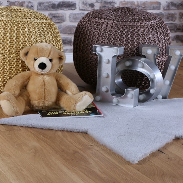 Wohnraumdekoration mit zwei Sitzpoufs, einem Teddybären, einem Buch und leuchtenden Buchstaben vor einer Ziegelwand auf einem weichen Vorleger.