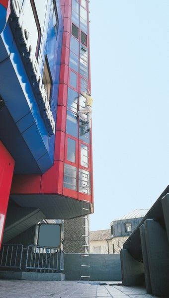 Eine Person steigt eine Notleiter an einem mehrstöckigen Gebäude hinauf.