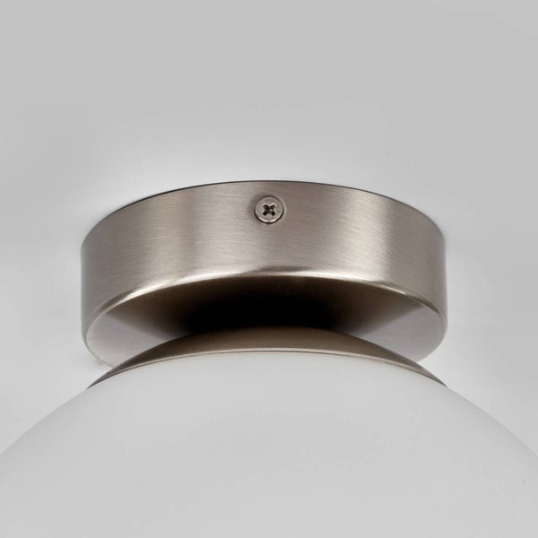Detailansicht einer runden Halterung aus gebürstetem Metall für eine Lampe mit weißem Glasschirm.