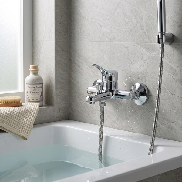 Verchromte Wannenarmatur mit Brausegarnitur an grauen Wandfliesen über einer gefüllten weißen Badewanne in einem hellen, modernen Badezimmer.