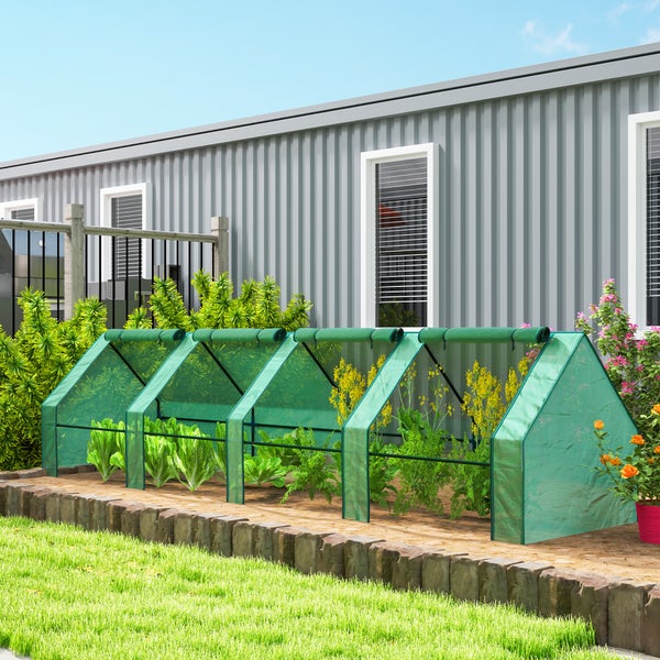Ein Folientunnel für Pflanzen im Garten vor einem Haus mit Gartenbeeten, der Schutz für Gemüse und Blumen bietet.