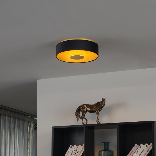 Runde Deckenleuchte mit schwarzem Textilschirm und goldener Innenseite über einem Regal mit Dekoration.