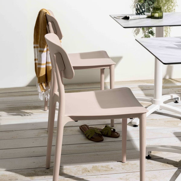 Moderne Gartenstühle aus Kunststoff in hellem Rosa neben einem weißen Tisch mit Marmoroptik auf einer hellen Holzterrasse.