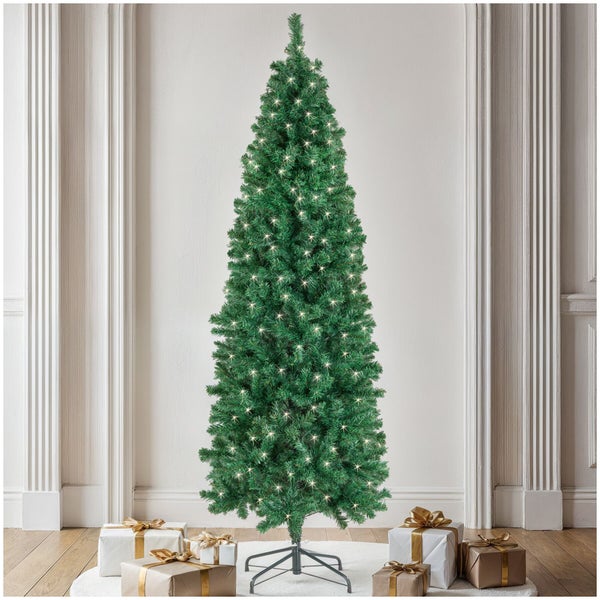 Ein hoher, schlanker künstlicher Weihnachtsbaum mit integrierter Lichterkette und Geschenken darunter in einem klassischen Wohnraum.